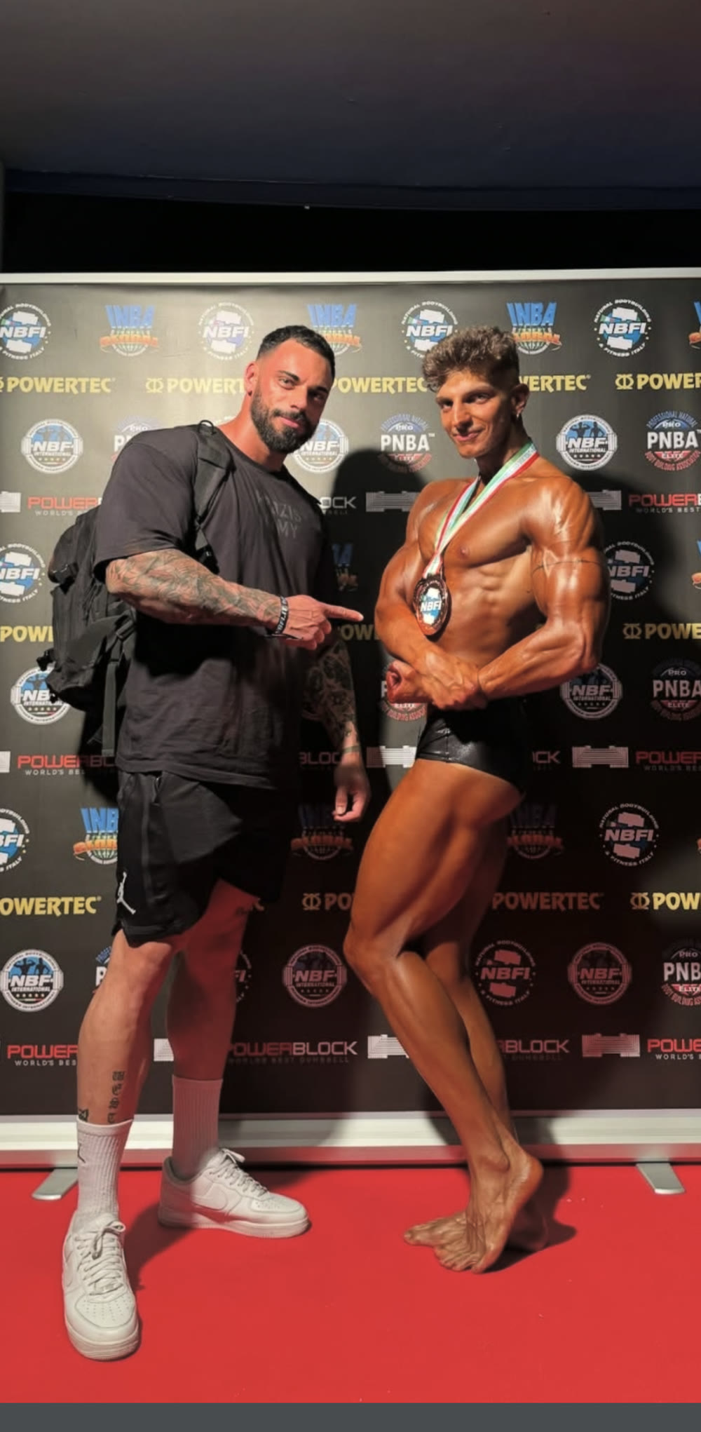 Riccardo Matterazzo indica il suo atleta, con la medaglia NBFI al collo, davanti al fondale della gara
